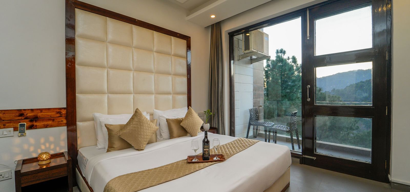 The premium room of DLS Whispering Winds with a bed, bed side tables, and a glass door leading to the balcony overlooking the mountain view